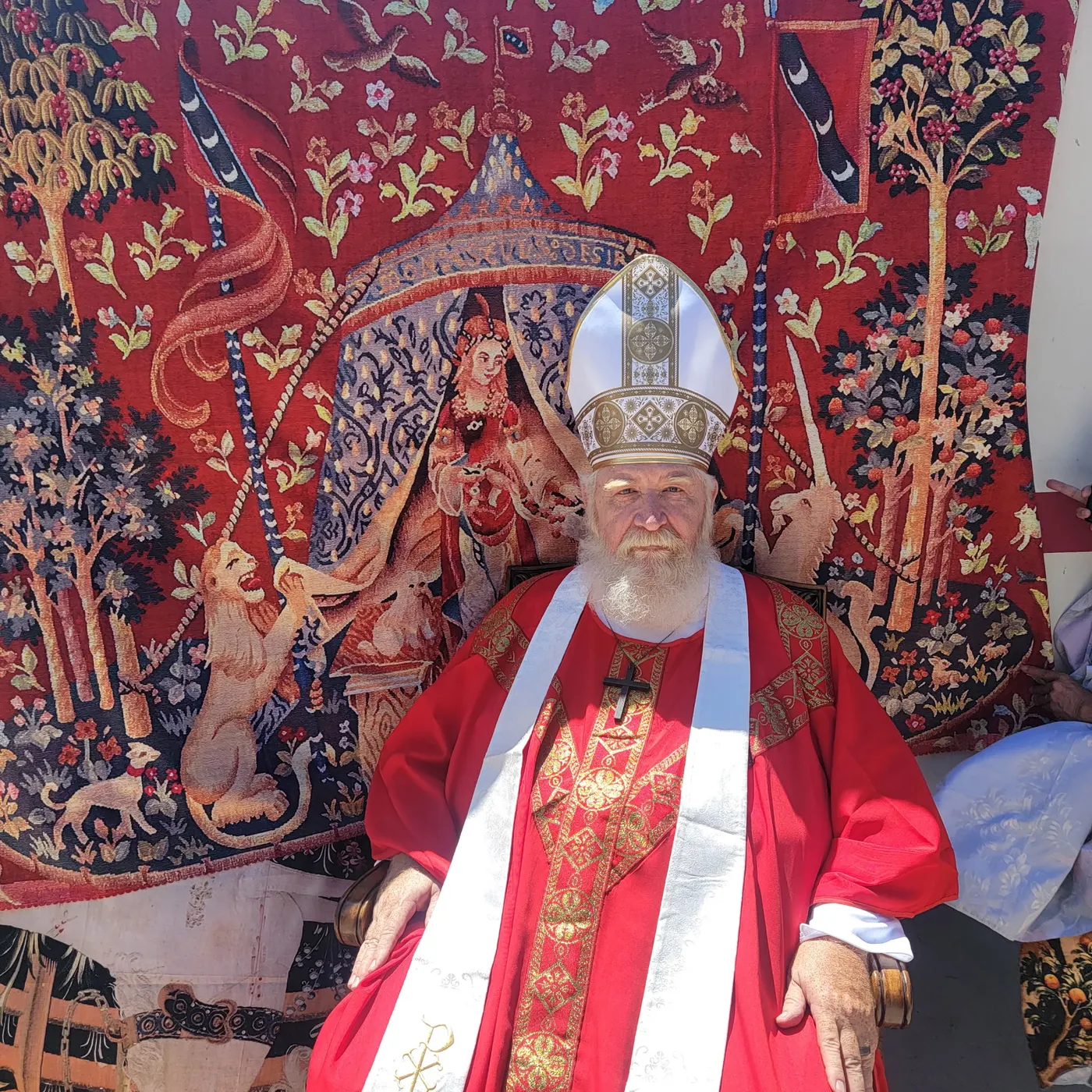St. Nicholas in mitre and red vestments, seated before a red medieval tapestry