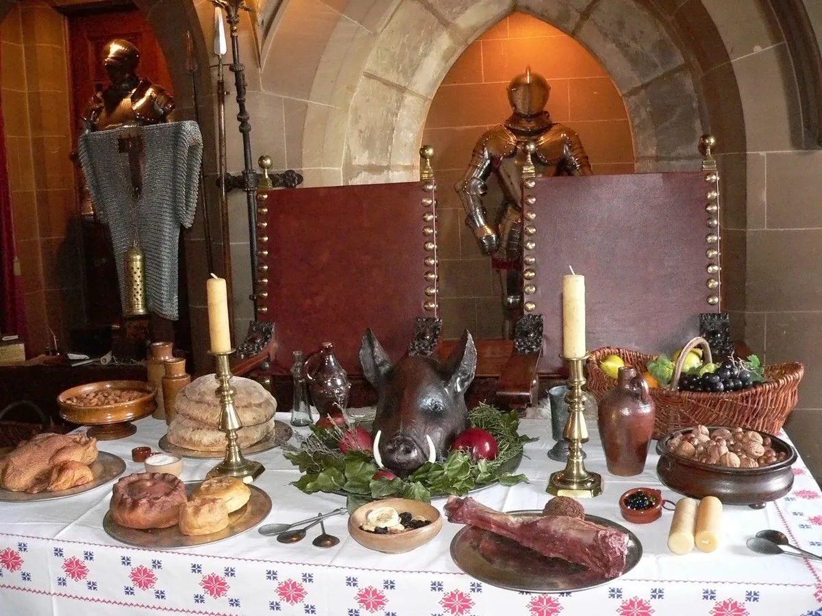 A medieval feast table laid with breads, pies and pewter in a candlelit hall